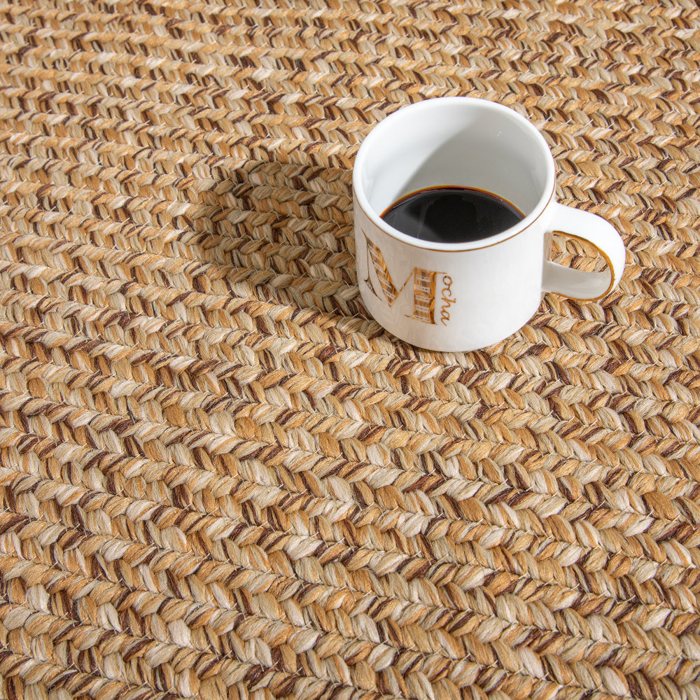 Tan hand-braided rug with coffee cup, ideal for indoor and outdoor spaces.