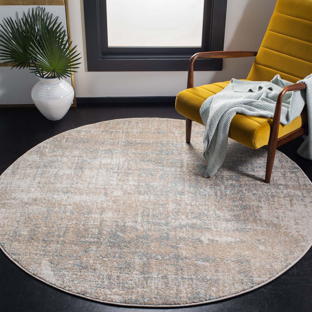 Round Harmonious Sunset Seren rug in soft colors beside modern chair and plant.