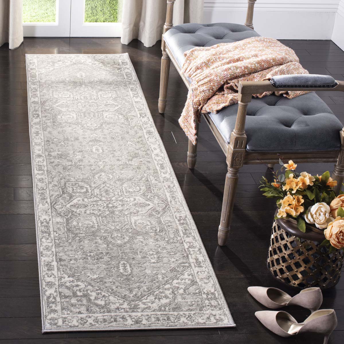 Light gray vintage runner rug beside tufted bench with throw and flowers.