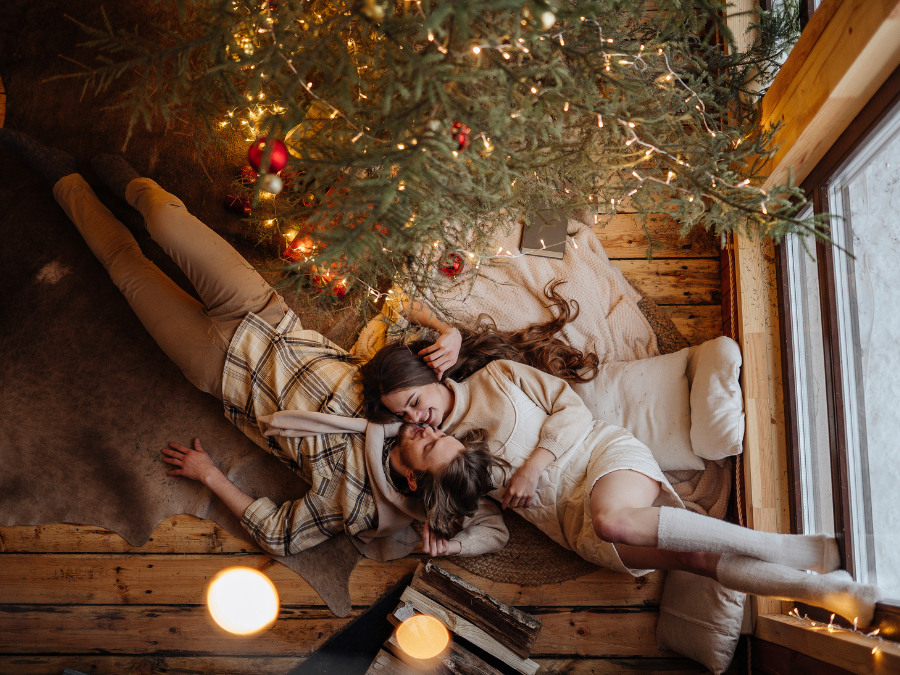 Couple relaxing by Christmas tree, lying comfortably on soft rugs.